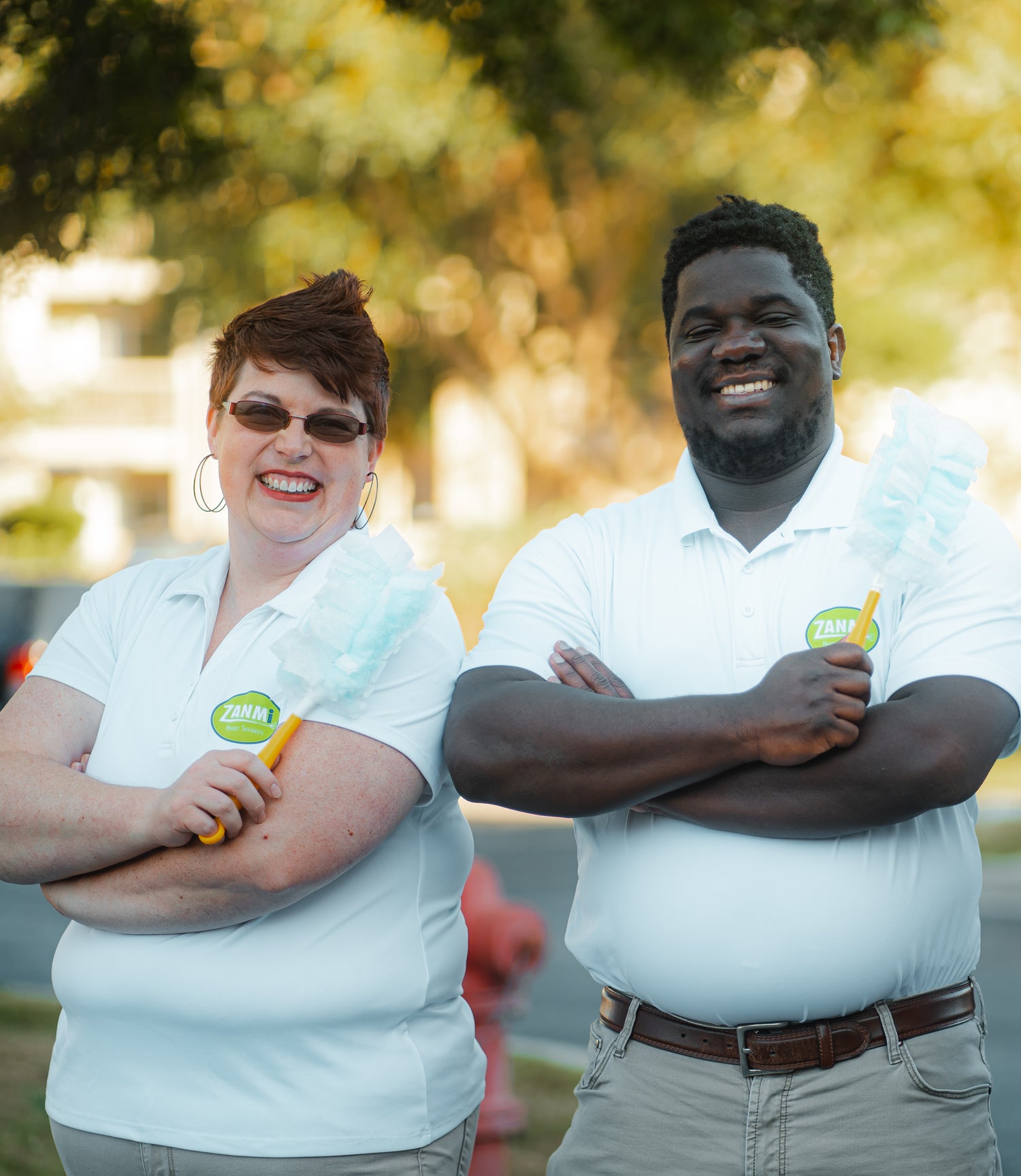 A husband and wife standing next to each other and smiling with trees in the background.