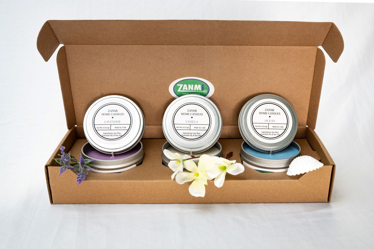 A cardboard box with three handmade soy wax candles and flowers inside.
